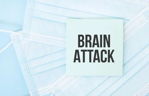 Piece of paper with phrase BRAIN ATTACK on pile of blue medical masks. Corona Stock Photos