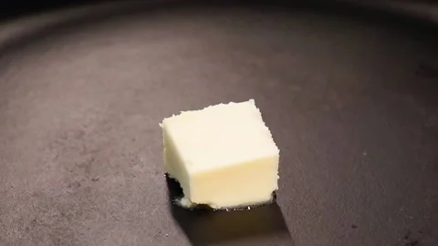 Piece pat of butter melting on a black cast iron frying pan, concept of cooking Stock Footage 227341653