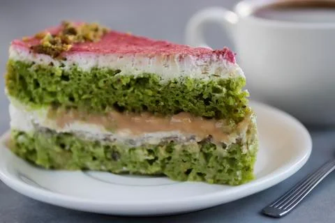 A piece of pistachio cake on a white plate and a cup of coffee. Stock Photos