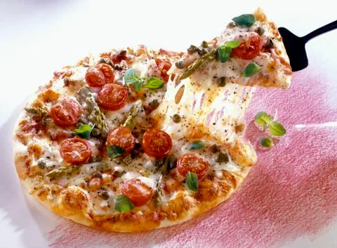 Piece of pizza pulling strands of cheese from vegetable pizza 写真素材