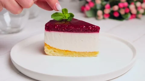 A piece of raspberry cake or cheesecake on a white plate garnished with mint Stock Footage 154631511