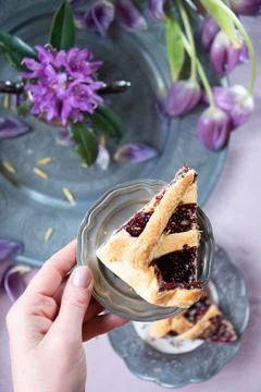 A piece of raspberry layer cake in a woman's hand Lilac spring tulips on a plate Stock Photos