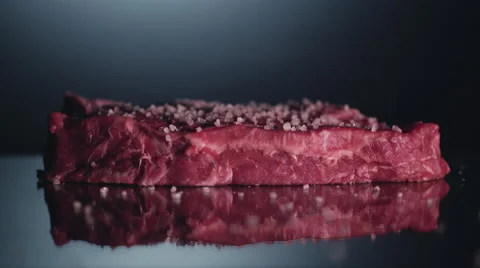 Piece of raw beef steak is cooking with salt and pepper. Close up. Macro lens Stock Footage 61942963