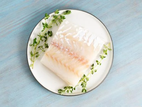 Piece of raw cod fish fillet on plate on blue wooden table, top view Stock Photos