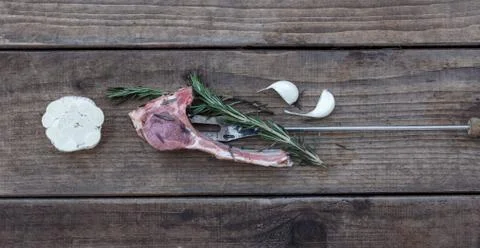 A piece of raw meat on a fork lying on rough wooden planks with garlic, top view Stock Photos