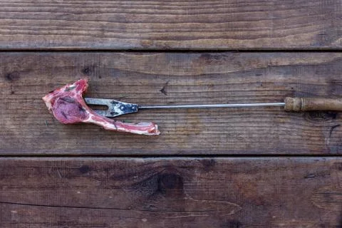 A piece of raw mutton on a fork lying on rough wooden planks, top view Stock Photos