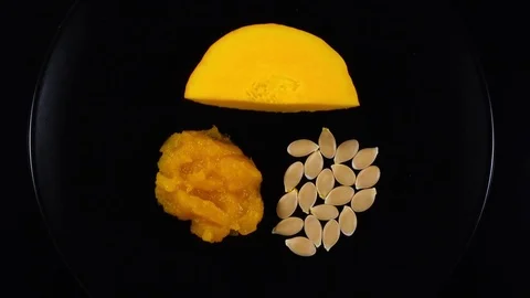 Piece of raw rip pumpkin rotates on black plate with squash soup and pepitas. 4K Vidéo 74060835