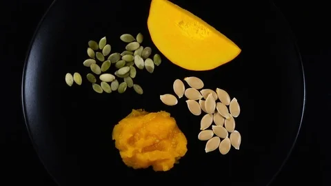 Piece of raw rip pumpkin rotates on black plate with squash soup and pepitas. 4K Видео 74060880