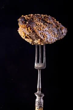 Piece of roasted meat on fork. Cold-boiled baked pork with mustard grains on  Stock Photos