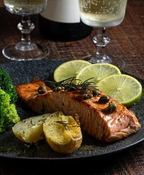 A piece of roasted salmon grilled lemon pepper and salt on a dark plate with Stock Photos