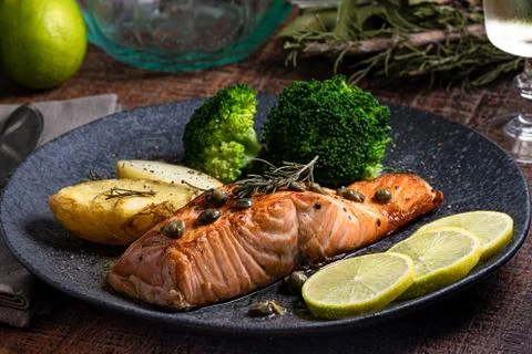 A piece of roasted salmon grilled lemon pepper and salt on a dark plate with Stock Photos