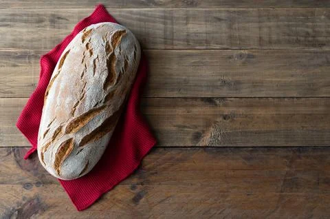 Piece of rustic bread on wooden background with red napkin ornament. Stock Photos