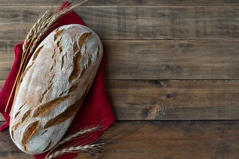 Piece of rustic bread on wooden background with ornaments of ears of wheat... Stock Photos