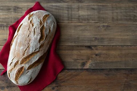 Piece of rustic bread on wooden background with red napkin ornament. Copy s.. Stock Photos
