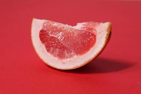 A piece of a slice of red grapefruit on a red background with a hard shadow.  Stock Photos