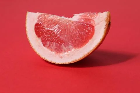 A piece of a slice of red grapefruit on a red background with a hard shadow.  Stock Photos