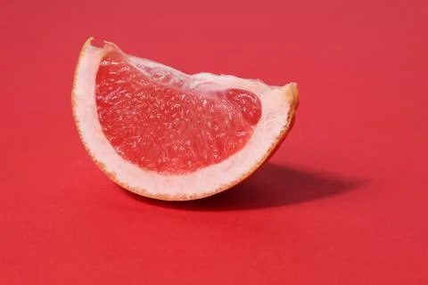 A piece of a slice of red grapefruit on a red background with a hard shadow.  Stock Photos
