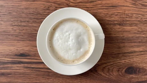 A piece of sugar falling into a cup of coffee on wooden table. Stock Footage 273773488