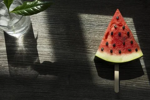 A piece of triangular watermelon on an ice cream stick and a glass of cold dr Stock Photos