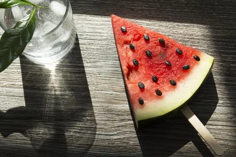 A piece of triangular watermelon on an ice cream stick and a glass of cold dr Stock Photos