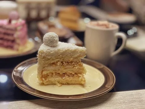 Piece of white cake with sponge cake, coconut flakes and decoration on top of Stock Photos