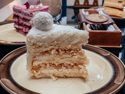 Piece of white cake with sponge cake, coconut flakes and decoration on top of Stock Photos
