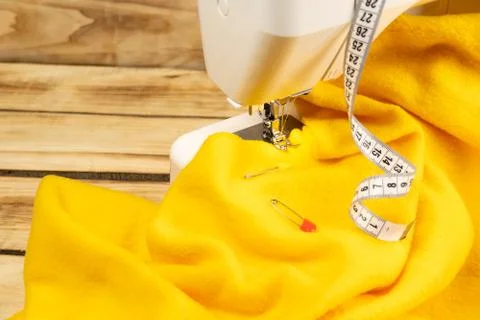 A piece of yellow fabric on a sewing machine and a centimeter on a wooden bac Stock Photos