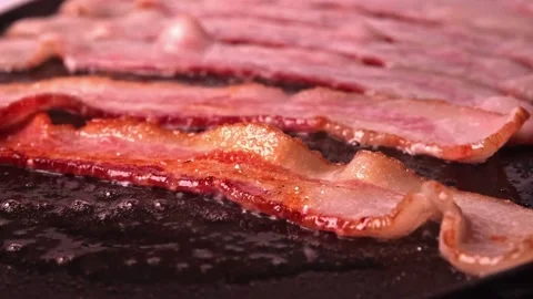 Pieces of bacon meat are fried in sizzling oil on hot skillet. 스톡 동영상 334643182