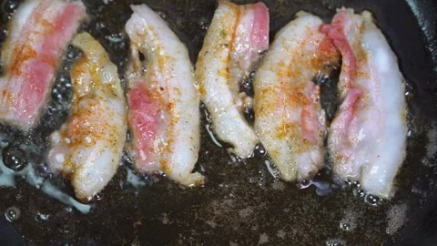 Pieces of bacon strips in a frying pan are fried in bubbles food of oil. 스톡 동영상 334642380
