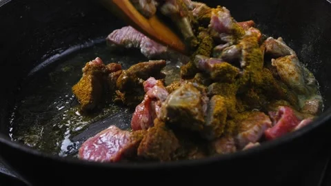 Pieces of beef are fried in a frying pan with oil and spices and turned over Stock Footage 262087155