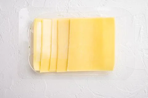 Pieces of Cheddar cheese, in plastic pack, on white stone background, top vie Stock Photos