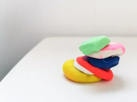 Pieces of colored plasticine collected in a pyramid on a white table. Stock Photos