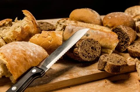 Pieces of cut and torn bread with a knife on wooden board. Stock Photos