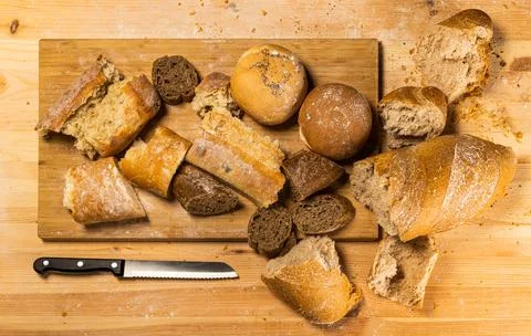 Pieces of cut and torn bread with a knife on wooden board. Stock Photos