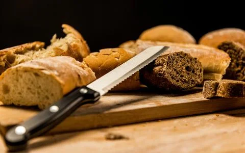 Pieces of cut and torn bread with a knife on wooden board. Stock Photos