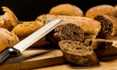 Pieces of cut and torn bread with a knife on wooden board. Stock Photos