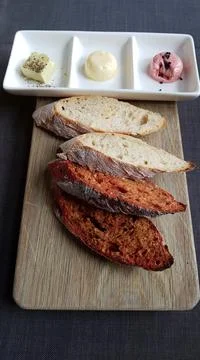 Pieces of different types of bread on a board and butter in a ceramic rosette Stock Photos
