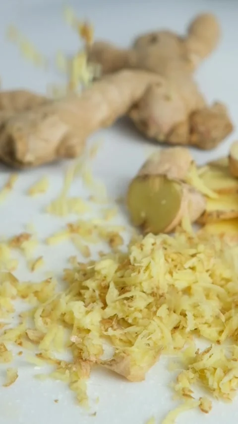 Pieces of finely grated fresh ginger root fall on kitchen board, vertical slow Stock Footage 276480965