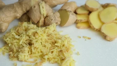 Pieces of finely grated fresh ginger root fall on kitchen board slow motion. Stock Footage 276536177