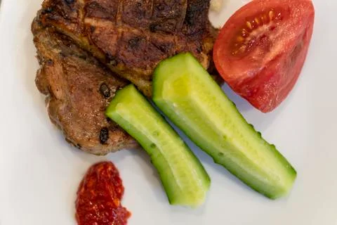 Pieces of fried meat on plates and tomatoes, cucumbers and red sauce. BBQ Stock Photos