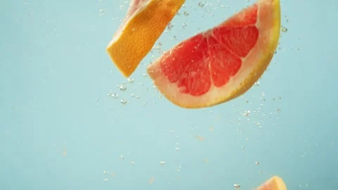 Pieces of grapefruit one by one fall into the water on a blue background. Stock Footage 263244546