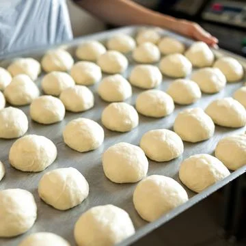Pieces of raw dough on baking sheet. Round buns, cooking process. Baker holding Stock Photos
