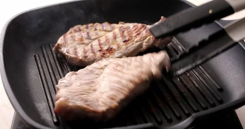 Pieces of raw meat are turned over on a grill pan using tongs. Stock Footage 250277226