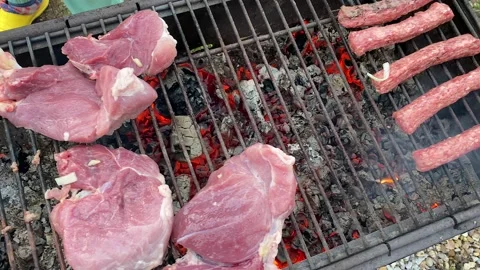 Pieces of raw red pork meat are laid out on a charcoal grill Stock-Footage 200493661