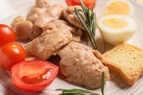 Pieces of tasty cod liver, tomatoes and herbs on white plate as background, c Stock Photos