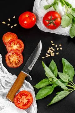 Pieces of tomatoes with basil branches, pine nuts and a knife Stock Photos