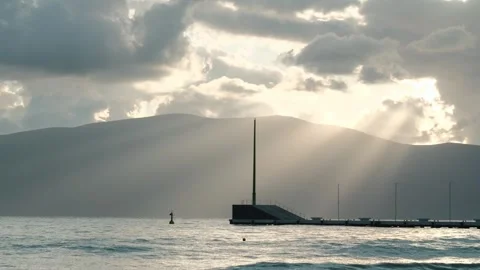 Pier and dramatic sun rays breaking through clouds above distant mountains Stock Footage 328103802