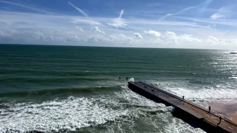 A pier extending into the ocean with waves crashing, under blue sky with clouds Stock Footage 280323229