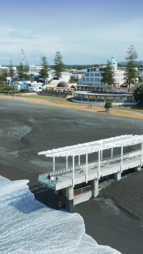 A pier extends over a black sand beach in Marine Parade, Napier, New Zealand 스톡 동영상 332955604