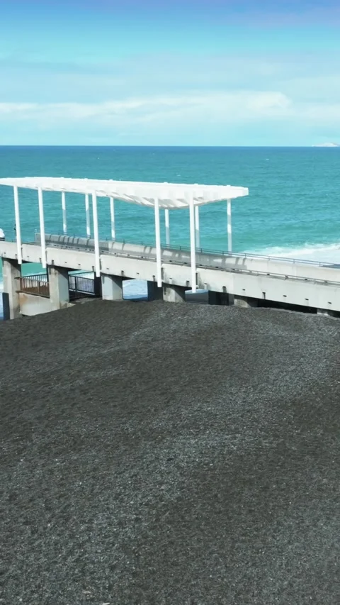 A pier extends over a black sand beach in Marine Parade, Napier, New Zealand Stock-Footage 332968538